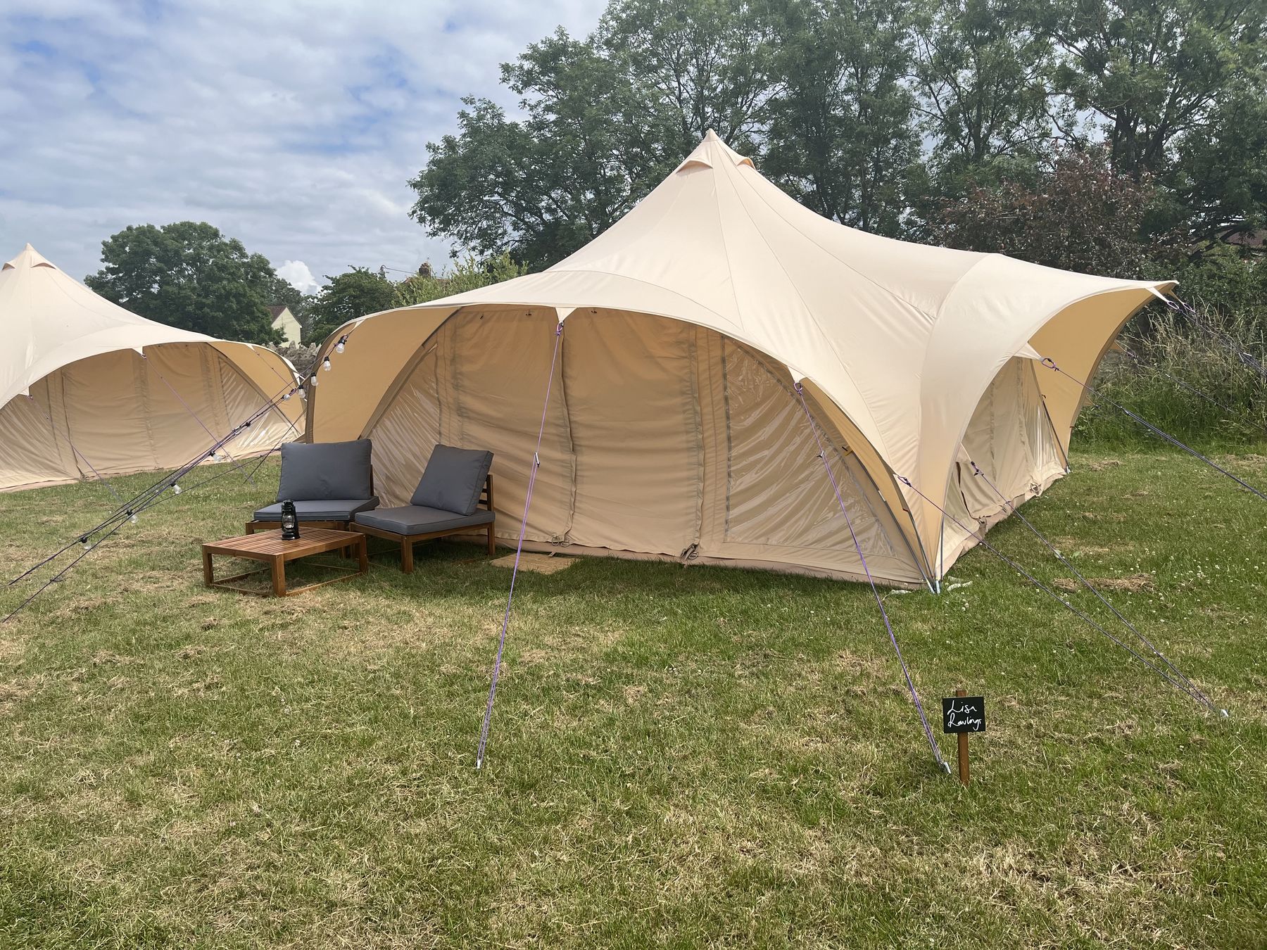 A cream canvas canopy and bell tent pitched on grass under a blue sky
